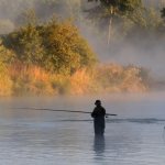 A man fishes in the fog.